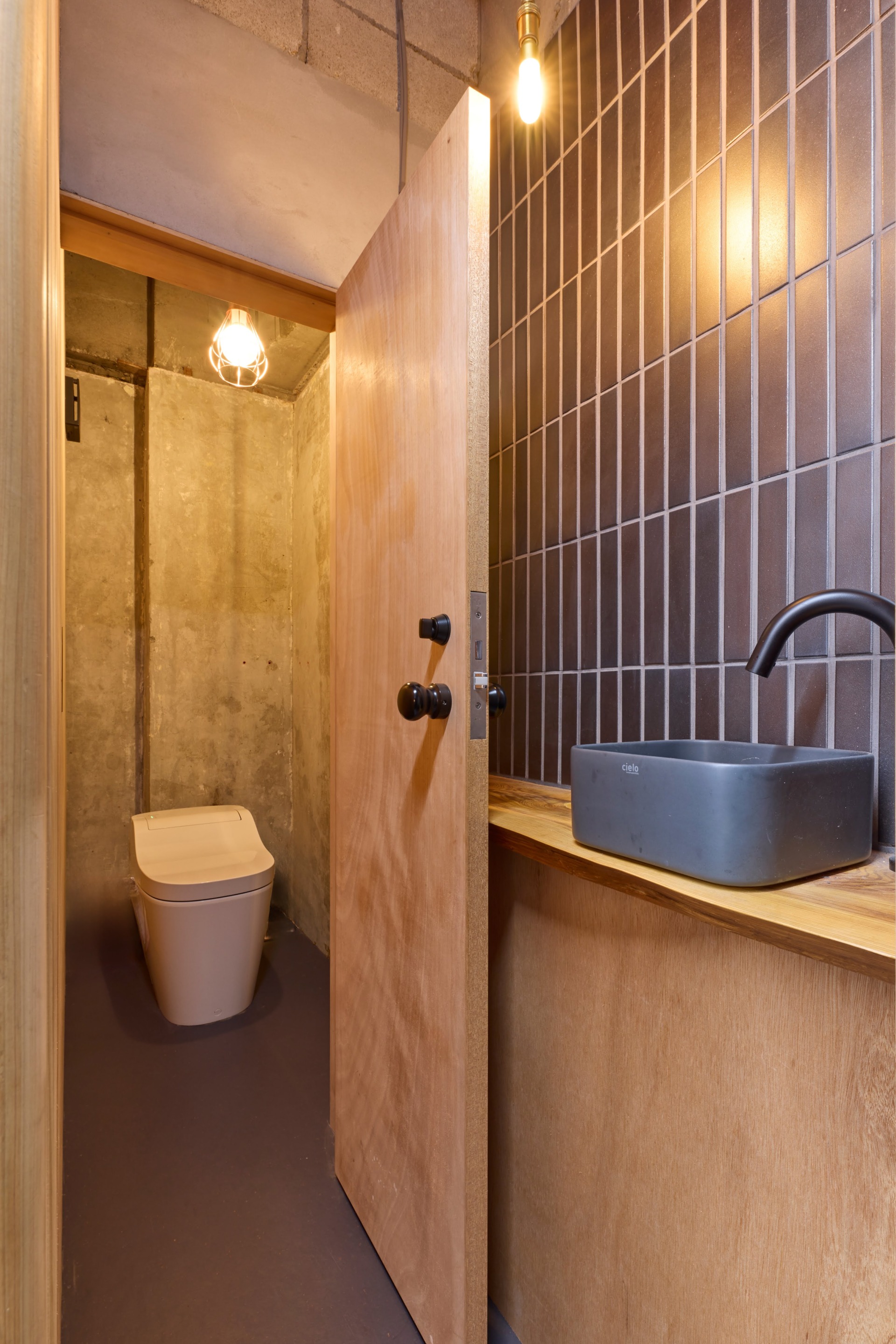 トイレ手前の手洗い器とタイルのクラフト感と、建具類の木そのままの素材感の組み合わせもユニーク