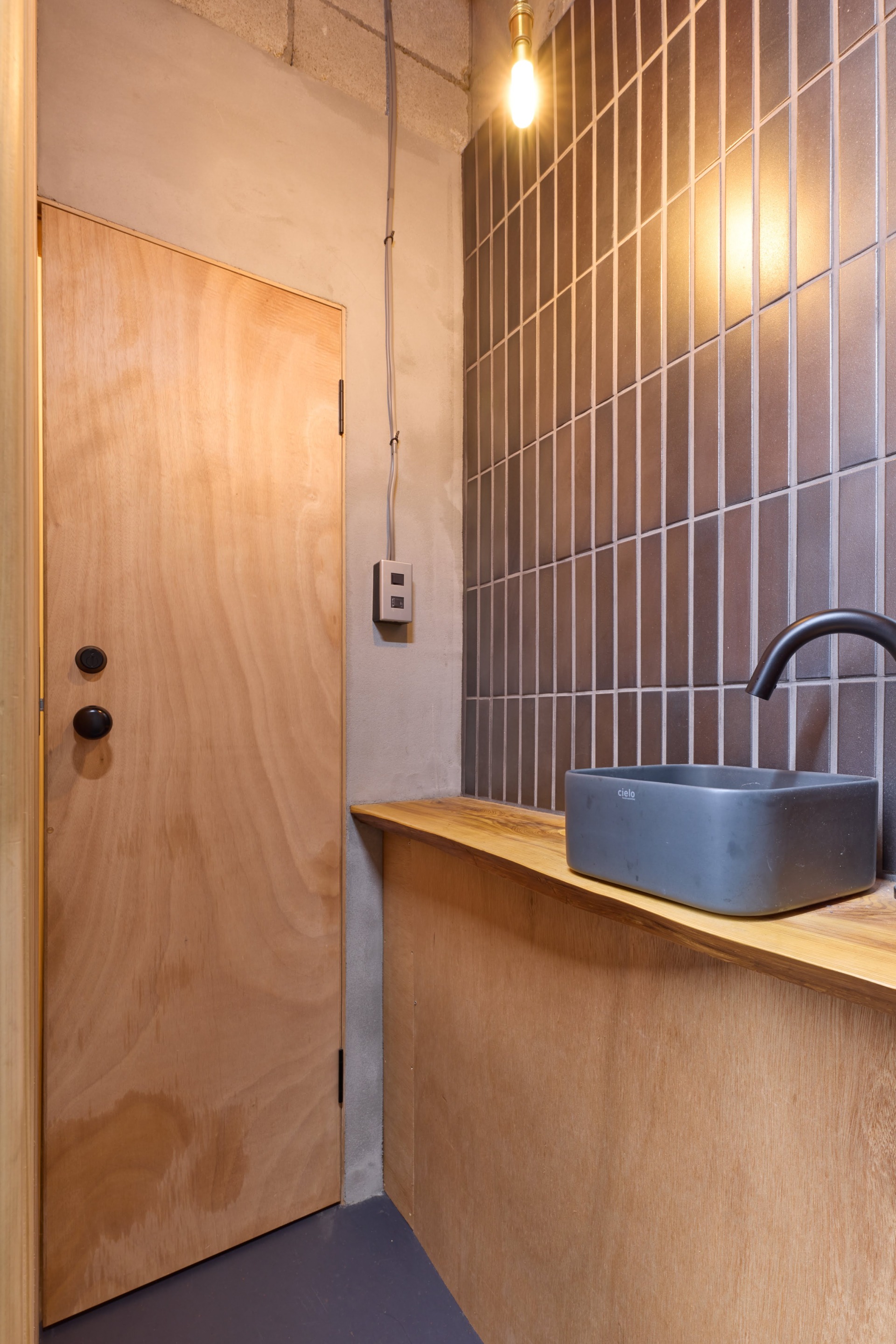 トイレ手前の手洗い器とタイルのクラフト感と、建具類の木そのままの素材感の組み合わせもユニーク